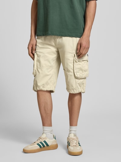 Męski model nosi Bermudas mit Pattentaschen und Logo-Stitching od Alpha Industries, bawełna, krój prosty, kieszenie boczne, szerokość w rozmiarze 32: 44 cm, długość wewnętrzna nogawki: 33 cm, zdjęcie całej sylwetki z przodu
