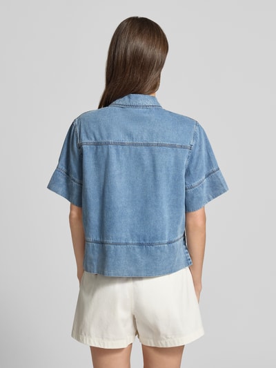 Frauenmodel trägt Boxy Fit Jeansbluse mit Brusttaschen Modell 'LAIKA' von SUNCOO PARIS aus Lyocell-Baumwoll-Mix, Rückenlänge 52 cm, Ärmellänge 24 cm, Hellblau mit sichtbaren Nähten, Ganzkörperansicht Rückansicht.