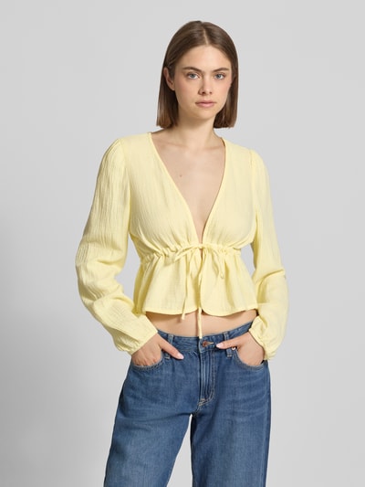 Frauenmodel trägt Regular Fit Langarmbluse aus reiner Baumwolle Modell 'SASTINA' von Pieces, Optik: Unifarben, Musselin, V-Ausschnitt, Bindeverschluss, Ärmelform: Langarm, blasses Gelb, strukturierte Oberfläche, Ganzkörperansicht von vorne.