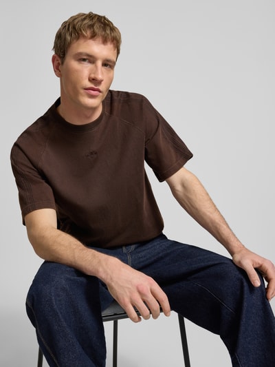 Männermodel trägt T-Shirt mit Rundhalsausschnitt und Label-Stitching von adidas Originals aus reiner Baumwolle, Relaxed-Fit, Nahaufnahme Oberkörper.