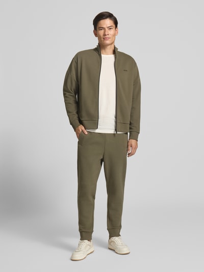 Männermodel trägt Regular Fit Sweatjacke aus Baumwoll-Mix Modell 'SW_Union Skaz' von BOSS, olivefarben, glatte Struktur, Ganzkörperansicht von vorne, Herren Sweatjacke von BOSS.