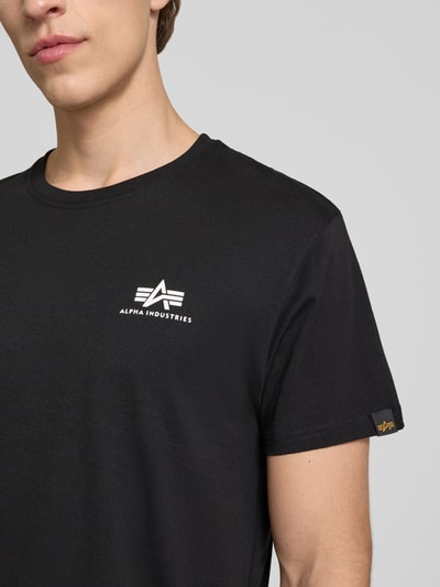 Männermodel trägt T-Shirt mit Logo und Rundhalsausschnitt von Alpha Industries aus Reine Baumwolle im Regular-Fit, Logo vorn, Nahaufnahme Oberkörper. Rückenlänge bei Größe M: 67 cm.