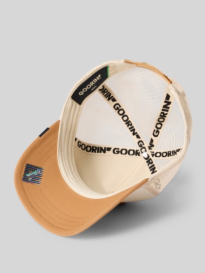 Produktfoto, Trucker Cap mit Motiv-Patch Modell 'The GOAT' von GOORIN BROS., aus Material-Mix mit Baumwoll-Anteil, verstärkter Schirm, Größenverstellbar, beigefarbene Mesh-Struktur mit kontrastfarbenem Schirm, Label-Details innen sichtbar.