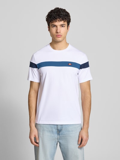Männermodel trägt Regular Fit T-Shirt mit Logo-Detail Modell 'Caserio' von Ellesse aus reiner Baumwolle, weiß mit blauen Streifen, Kurzärmelig, Rundhalsausschnitt, Rückenlänge bei Größe M 68 cm, Ganzkörperansicht von vorne.