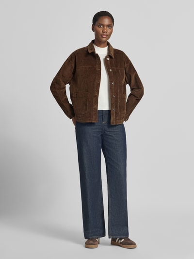 Frauenmodel trägt Relaxed Fit Langarmbluse aus reiner Baumwolle Modell 'JAMIE' von VERO MODA in Dunkelbraun zu blauer Hose, neutrale Farben, weiche Textur, Ganzkörperansicht von vorne.
