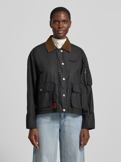 Modelka nosi Jacke aus Baumwolle mit Pattentaschen von Original Bombers, czarna bawełna, krój regular fit, wykładany kołnierz, kieszenie z patką, listwa guzikowa, długość tyłu w rozmiarze S: 60 cm, szerokość ramion w rozmiarze S: 52 cm, szerokość klatki piersiowej w rozmiarze S: 58 cm, długość rękawów w rozmiarze S: 57 cm, widok całej sylwetki z przodu