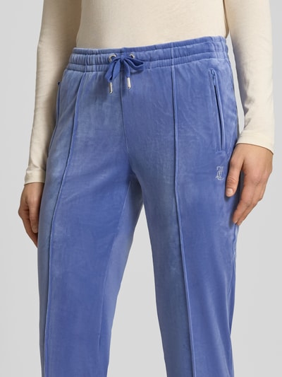 Kobiece model nosi spodnie dresowe z długimi szwami model 'TINA' od Juicy Couture, mieszanka materiałów z dodatkiem streczu, krój regular fit, elastyczny pas, długość wewnętrzna nogawki 80 cm przy rozmiarze S, niebieski, zbliżenie na górną część nóg.