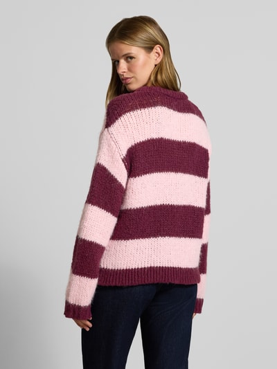Frauenmodel trägt Relaxed Fit Pullover im Chunky Knit Look Modell 'DORTHEA' von PIECES, breite rosa und bordeauxfarbene Streifen, Grobstrick, Ganzkörperansicht Rückansicht. Damen Pullover von PIECES.