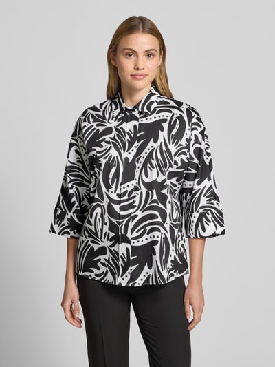 Frauenmodel trägt Bluse mit verdeckter Knopfleiste und 3/4-Arm von Christian Berg Woman, schwarz-weiß gemustert, Regular Fit, reine Baumwolle, Hemdblusenkragen, abgerundeter Saum, Ganzkörperansicht von vorne.