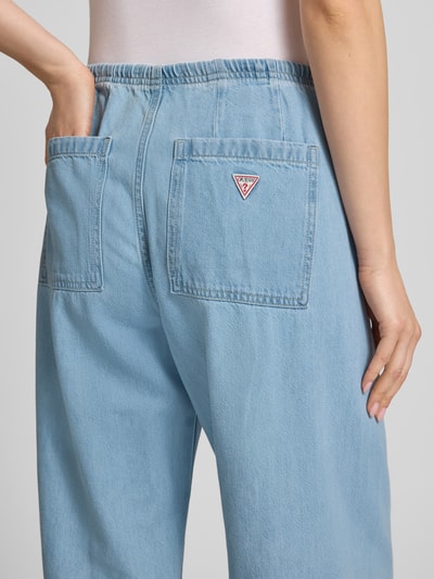 Frauenmodel trägt Low Rise Jogpants mit weitem Bein von Guess Jeans im Baumwoll-Lyocell-Mix, hellblaue Jeans-Optik, Detailaufnahme Rückansicht.