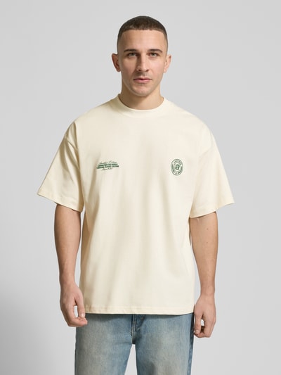 Männermodel trägt T-Shirt aus Baumwolle Modell 'Sunday Miles' von ANOTHER COTTON LAB in Beige mit grünen Label-Details, Ganzkörperansicht von vorne.
