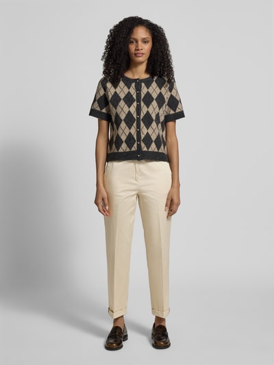 Modelka nosi Slim Fit Chino aus Baumwoll-Satin od s.Oliver BLACK LABEL, jasny beż, satynowy bawełniany materiał, krój slim fit, kanty, elastyczny pas, kieszenie boczne oraz imitacja kieszeni z tyłu, długość do kostek z mankietem; widok całej sylwetki z przodu.