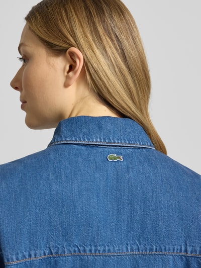 Kobiece model prezentuje Regular Fit Jeansbluse aus reiner Baumwolle od Lacoste, tkanina stylizowana na denim, wyhaftowane logo, krój regular fit, widok z tyłu zbliżenie.