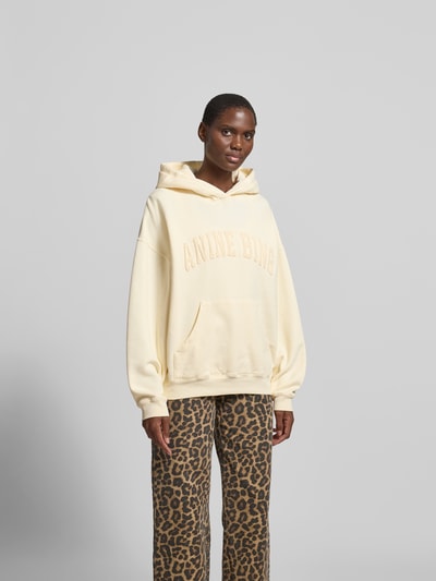 Frauenmodel trägt Oversized Hoodie aus reiner Baumwolle von Anine Bing in Creme mit Känguru-Tasche, Label-Detail, elastischen Abschlüssen, Rückenlänge bei Größe S 63 cm, Ganzkörperansicht von vorne.