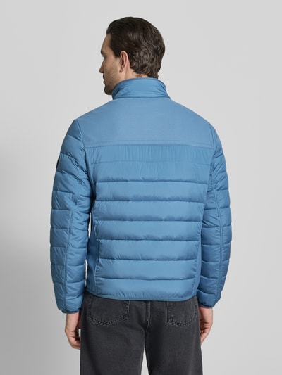 Męski model nosi Regular Fit Steppjacke mit seitlichen Stretcheinsätzen od Tom Tailor, jednolity kolor, krój regular fit, stójka, zamek błyskawiczny, naszywka z logo, pas na plecach, boczne elastyczne wstawki, długi rękaw, elastyczne zakończenie, funkcja: hydrofobowy, kieszeń wewnętrzna, boczne kieszenie na zamek, brustasza; widok całej sylwetki od tyłu.