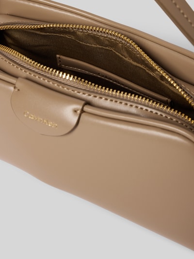 Produktfoto, Torebka 'Handtasche mit Label-Detail und Schulterriemen' od CK Calvin Klein, główna przegroda z zamkiem błyskawicznym, detal z logo, uchwyt, pasek na ramię, szerokość w rozmiarze 1: 24 cm, długość w rozmiarze 1: 14 cm, głębokość w rozmiarze 1: 7 cm, długość paska na ramię w rozmiarze 1: 110 cm, beżowy kolor, gładka faktura, zaokrąglone kształty.