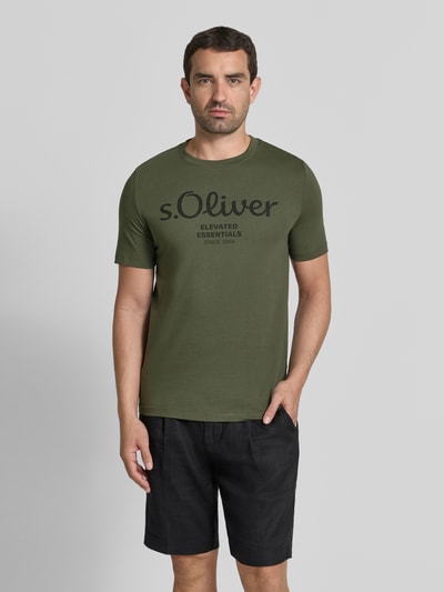 Męski model nosi Regular Fit T-Shirt aus reiner Baumwolle Modell 'BASIC TEE BIG LOGO' von s.Oliver RED LABEL, oliwkowa zieleń, czarny nadruk, prosta faktura, Ganzkörperansicht von vorne.