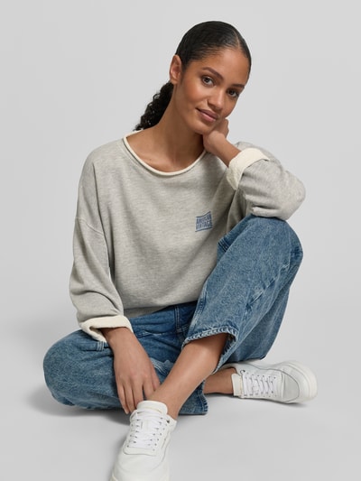 Frauenmodel trägt Oversized Sweatshirt mit Label-Print von American Vintage, hellgrau, Baumwoll-Mix, Rundhalsausschnitt, Jeans, Nahaufnahme Oberkörper.