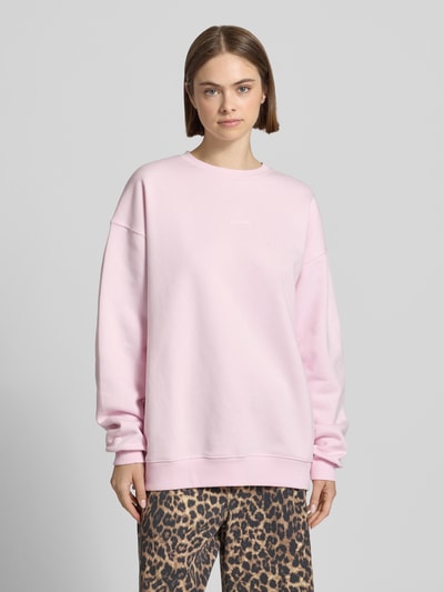 Frauenmodel trägt Oversized Sweatshirt mit Logo-Print von OH APRIL in zartem Rosa, aus Baumwoll-Mix, Oversized-Fit, gerippter Rundhalsausschnitt, überschnittene Schultern, Logo-Print auf der Brust, glatte Textur, Ganzkörperansicht von vorne.