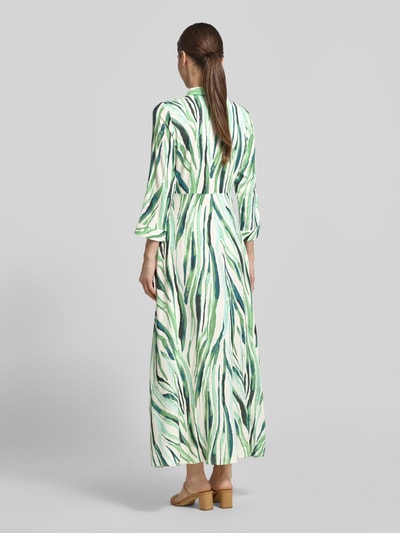 Frauenmodel trägt Hemdblusenkleid aus Viskose Modell 'SAVANNA' von YAS mit grün-weißem Muster, Midikleid, Taillierter Passform, Kentkragen, Knopfleiste, 3/4-Arm, Rückenlänge bei Größe S: 135 cm, Brustweite: 42 cm, Ärmellänge: 49 cm, Ganzkörperansicht Rückansicht.