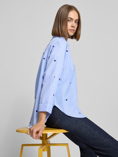 Modelka kobieca nosi bluzkę koszulową Boxy Fit Hemdbluse mit Baumwoll-Anteil Model 'NEW LINA GRACE' od ONLY, Wzór na całej powierzchni, wzór w paski, wyhaftowany motyw, kołnierzyk koszulowy, długi rękaw, wykończenie materiału: bawełna, widoczne jasnoniebieskie i granatowe odcienie, tekstura tkaniny, widoczne motywy, zdjęcie z boku, ujęcie całej sylwetki.