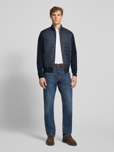 Męski model nosi Regular Fit kurtkę w stylu pikowanym Model 'Selanik' od bugatti, mieszanka bawełny, stójka, wpuszczane kieszenie z zamkiem błyskawicznym, zamek błyskawiczny, elastyczne wykończenia, długość tyłu przy rozmiarze M: 70 cm, długość rękawów przy rozmiarze M: 69 cm, granatowe odcienie, prosty fason, tekstura gładka z pikowaniem, widok całej sylwetki z przodu.
