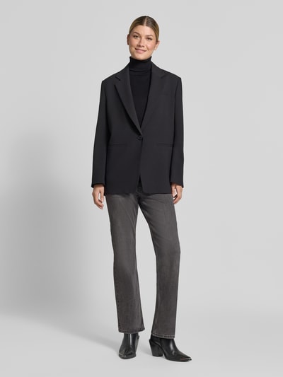 Frauenmodel trägt Bootcut Fit Jeans aus elastischem Baumwoll-Mix von Christian Berg Woman in Grau, kombiniert mit schwarzem Blazer und Boots, Ganzkörperansicht von vorne. Damen Jeans, 5-Pocket-Design, Gürtelschlaufen, Knopf- und Reißverschluss, Bundweite 38 cm, Innenbeinlänge 77 cm.
