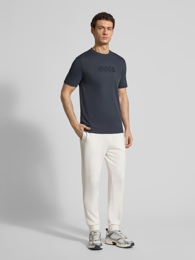 Männermodel trägt Regular Fit T-Shirt aus reiner Baumwolle Modell 'TS_TERRACE' von BOSS Green in Dunkelblau, unifarben, mit 3D-Label Print, jerseyartiger Struktur, Kurzarm und Rundhalsausschnitt, Ganzkörperansicht von vorne.