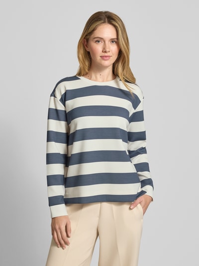Modelka nosi Bluza z okrągłym dekoltem od Christian Berg Woman, mieszanka materiałów z domieszką modalu, krój relaxed fit, wzór na całej powierzchni, jasnoniebieskie i kremowe szerokie pasy, gładka tekstura, zdjęcie całej sylwetki z przodu.