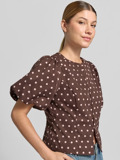 Vrouwenmodel draagt blouse met korte mouwen met ballonmouwen Model 'ANELA' van Neo Noir, nauwsluitende pasvorm, ronde hals, doorlopende haakjessluiting, bruin met lichtroze stippen, detailopname bovenlichaam.