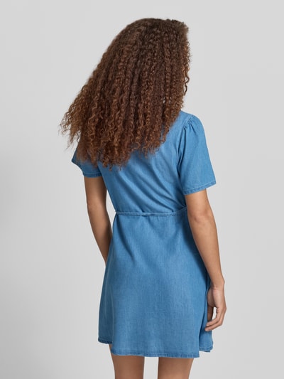 Frauenmodel trägt Tailliertes Jeanskleid aus Baumwoll-Lyocell-Mix Modell 'EVIDA-BEA' von Only in Denim-Optik, Mini-Länge, Kurzarm, Ganzkörperansicht Rückansicht.