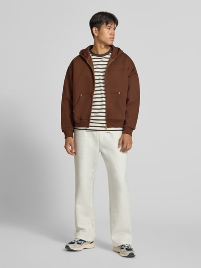 Männermodel trägt dunkelbraune Sweatjacke mit Kapuze von ANOTHER COTTON LAB, lockerer Schnitt, Zwei-Wege-Reißverschluss, Ganzkörperansicht von vorne