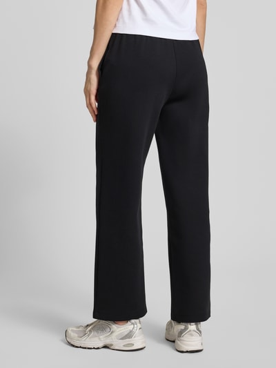 Frauenmodel trägt Sweatpants mit elastischem Bund und Logo-Print von ARMANI EXCHANGE in Schwarz mit seitlichen Eingrifftaschen, Ganzkörperansicht Rückansicht. Damen Sweatpants Straight Fit, Innenbeinlänge bei Größe S: 72 cm.
