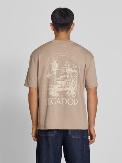 Männermodel trägt Oversized T-Shirt mit Backprint und Rundhalsausschnitt von PEGADOR, reine Baumwolle, beige Farbton, Rückenlänge 68 cm, Ganzkörperansicht Rückansicht.