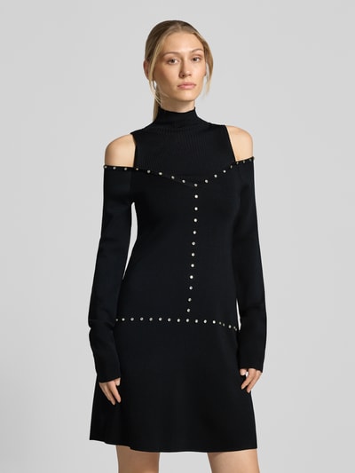 Modelka kobieca nosi sukienkę mini z mieszanki wiskozy Model 'Abito Maglia Corto' od Liu Jo White, czarna, ozdobne kamienie, wycięcia, stójka, długie rękawy, dopasowany krój, widok całej sylwetki z przodu.