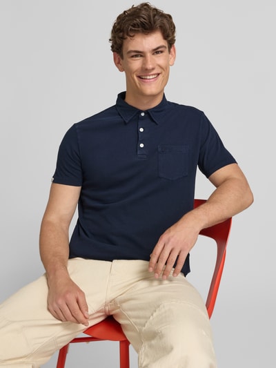 Männermodel trägt Slim Fit Poloshirt mit Brusttasche von Superdry in Dunkelblau, Baumwoll-Leinen-Mix, Knopfleiste, Rückenlänge 67 cm, Nahaufnahme Oberkörper.