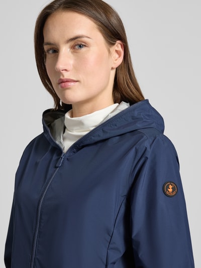 Frauenmodel trägt Regular Fit Jacke mit Zweiwegereißverschluss Modell 'Stella' von SAVE THE DUCK in Dunkelblau, Nahaufnahme Oberkörper. Damenjacke mit Eingrifftaschen, 60 cm Rückenlänge, 42 cm Schulterbreite, 52 cm Brustweite, 64 cm Ärmellänge.