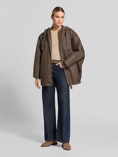 Frauenmodel trägt Relaxed Fit Mantel mit Kapuze Modell 'PURE' von g-lab in Braun, kombiniert mit Jeans und beigem Oberteil, Ganzkörperansicht von vorne. Damen Mantel mit Tunnelzug, Eingrifftaschen, Rückenlänge 69 cm, Schulterbreite 45 cm, Brustweite 88 cm, Ärmellänge 60 cm.