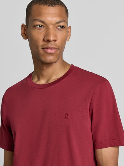Männermodel trägt Regular Fit T-Shirt aus reiner Baumwolle Modell 'JAAMES' von ARMEDANGELS in Dunkelrot, Nahaufnahme Oberkörper.