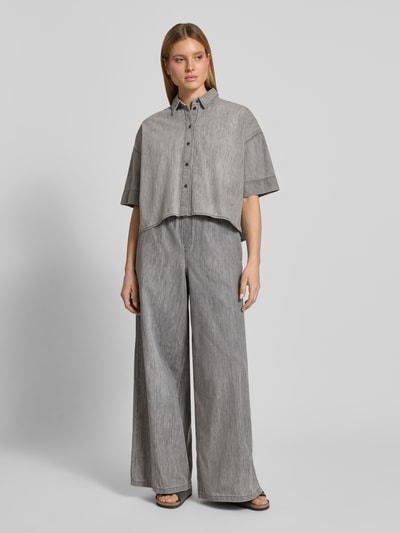 Kobiece model prezentuje spodnie materiałowe Wide Fit Stoffhose mit Rüschenbesatz Modell 'Dwindle' od Drykorn z czystej bawełny, krój wide fit, obszycie falbanami, elastyczny pas z tunelem, wpuszczane kieszenie, szerokość w rozmiarze 27/34: 37 cm, długość wewnętrzna nogawki w rozmiarze 27/34: 82 cm, szare odcienie, proste linie, lekko widoczna tekstura materiału, pełny widok z przodu.