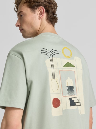 Męski model nosi Relaxed Fit T-Shirt aus reiner Baumwolle Modell 'NORMAN' von Selected Homme, jasny kolor, geometryczne nadruki na plecach, męski t-shirt, tylny widok całej sylwetki.
