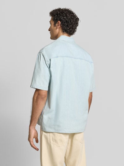 Männermodel trägt Regular Fit Jeanshemd aus reiner Baumwolle Modell 'CAMICIA' von Armani Exchange in Hellblau, Rückansicht Ganzkörperansicht. Kurzärmliges Design, Kentkragen, Zweiwege-Reißverschluss, dezentes Brand-Stitching, robustes Material, glatte Textur.
