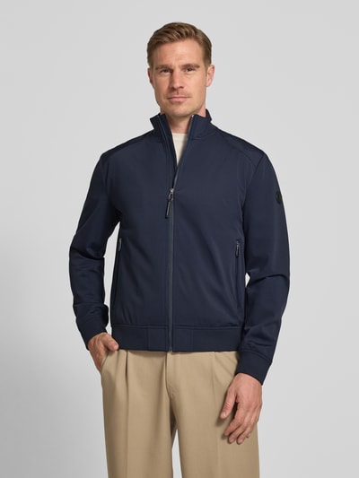 Męski model nosi kurtkę Jacke mit Stehkragen und Reißverschlusstaschen Modell 'Pablo' von JOOP! Collection, mieszanka materiałów z dodatkiem streczu, krój regular fit, stójka, kieszenie zapinane na zamek błyskawiczny, długość tyłu w rozmiarze 50: 66 cm, szerokość ramion w rozmiarze 50: 45 cm, szerokość klatki piersiowej w rozmiarze 50: 56 cm, długość rękawów w rozmiarze 50: 65 cm, granatowy kolor, proste linie, gładka tekstura, całkowity widok z przodu