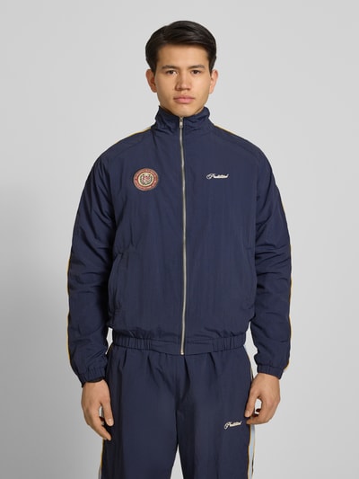 Männermodel trägt dunkelblaues Trackjacket mit Label-Stitching Modell 'Slipstream' von PROHIBITED, Relaxed Fit, Stehkragen, Reißverschluss, Ganzkörperansicht von vorne.