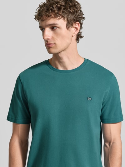 Männermodel trägt T-Shirt aus Baumwolle mit Rundhalsausschnitt von Christian Berg Men in Türkis, Regular-Fit, Label-Detail, Nahaufnahme Oberkörper. Rückenlänge bei Größe M: 71 cm, Reine Baumwolle.