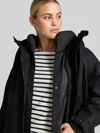 Frauenmodel trägt Regular Fit Mantel mit Stehkragen Modell 'Joy' von g-lab, schwarze glatte Struktur, Nahaufnahme Oberkörper. Damen Mantel mit Tunnelzug, Zweiwege-Reißverschluss, Rückenlänge 90 cm, Schulterbreite 56 cm, Brustweite 66 cm, Ärmellänge 52 cm.