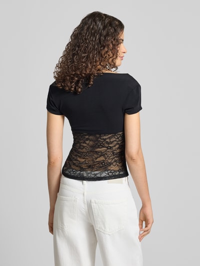 Frauenmodel trägt T-Shirt mit V-Ausschnitt und Spitze von Gina Tricot in Schwarz, Material-Mix mit Stretch-Anteil, Slim-Fit, Rückenlänge 51 cm, Spitze im Rückenbereich, Ganzkörperansicht Rückansicht.