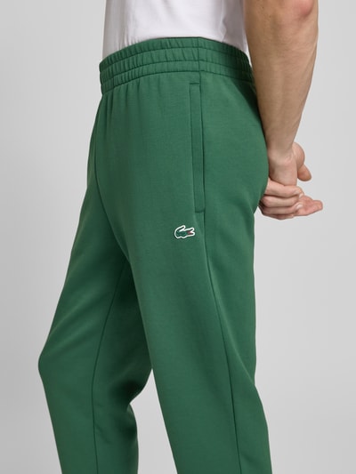 Mężczyznamodel nosi Tapered Sweatpants mit Baumwoll-Anteil od Lacoste Sport, zielony, logo-patch, elastyczny pas, scuba, zdjęcie z boku.