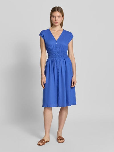 Modelka kobieca ma na sobie Knielanges Kleid aus Leinen-Mix mit Knopfleiste od Christian Berg Woman Selection, niebieski len z wiskozą, krój taliowany, długość do kolan, dekolt V, listwa guzikowa, krótkie rękawy z wykończeniem, detale smok, długość tyłu w rozmiarze 36: 44 cm, szerokość w rozmiarze 36: 44 cm, widok całej sylwetki z przodu.