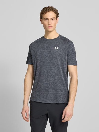 Männermodel trägt Herren T-Shirt mit Label-Print Modell 'Tech' von Under Armour, Grautöne, strukturierte Optik, Gerader-Schnitt, Rundhalsausschnitt, Rückenlänge bei Größe M 75 cm, Ganzkörperansicht von vorne.